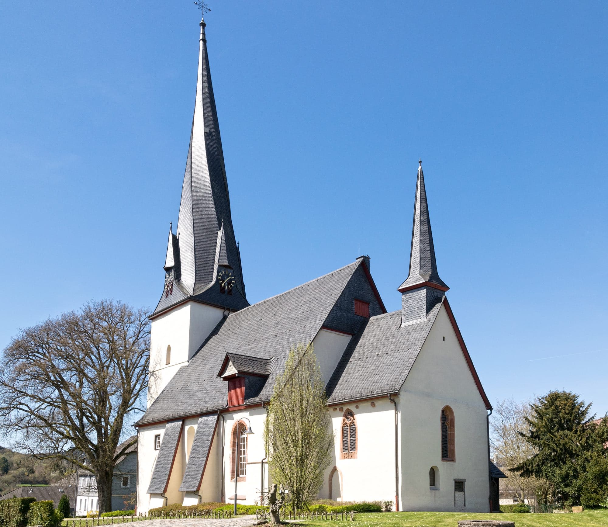 Evangelische Kirche in Breidenbach mit spitzem Turmhelm unter blauem Himmel